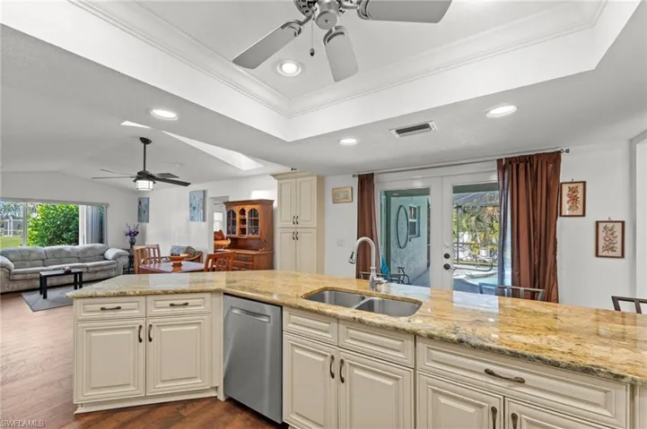 Kitchen with a ceiling fan, ornamental molding, open floor plan, a tray ceiling, and light stone countertops