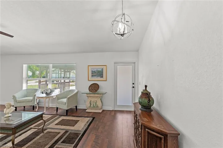 Living area featuring dark wood-style flooring, lofted ceiling, a ceiling fan, and a textured wall
