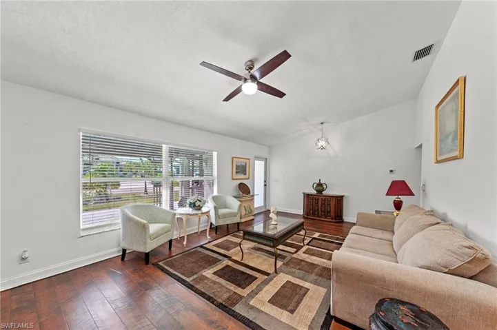 Living room with ceiling fan, dark wood finished floors, and a chandelier