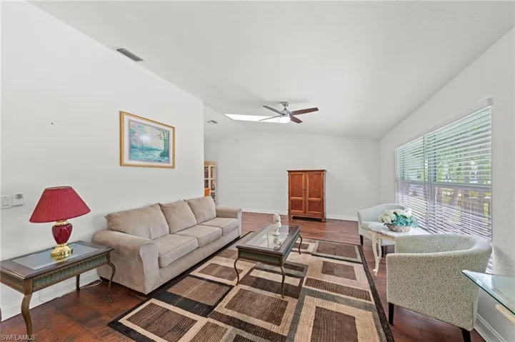 Living area with dark wood-style flooring, a ceiling fan, and lofted ceiling