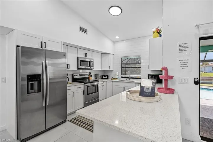 Kitchen with stainless steel appliances, a peninsula, light stone countertops, backsplash, and white cabinetry