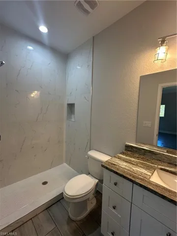 Bathroom featuring a tile shower, vanity, and toilet