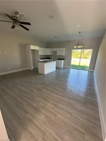 Unfurnished living room with ceiling fan with notable chandelier, light hardwood / wood-style floors, and sink