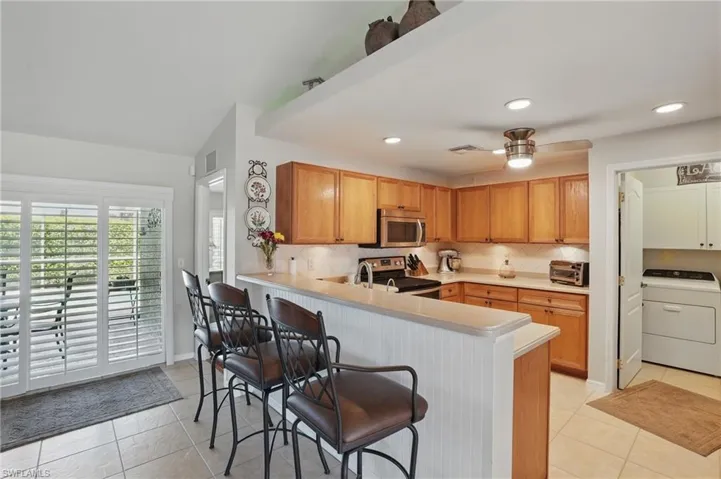 Kitchen featuring washer / clothes dryer, stainless steel appliances, light tile patterned floors, a breakfast bar, and recessed lighting