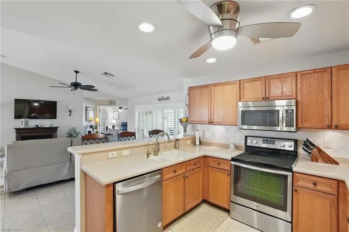 Kitchen featuring appliances with stainless steel finishes, a ceiling fan, a sink, open floor plan, and a peninsula