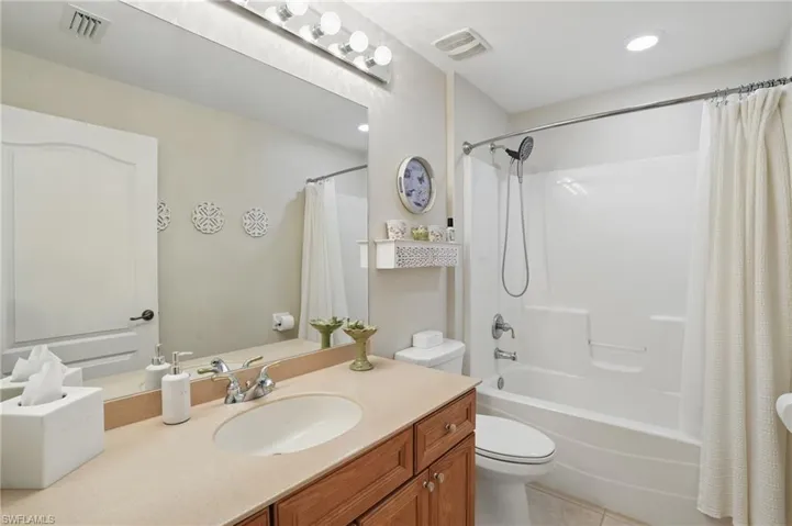 Bathroom with toilet, shower / bathtub combination with curtain, tile patterned flooring, and vanity
