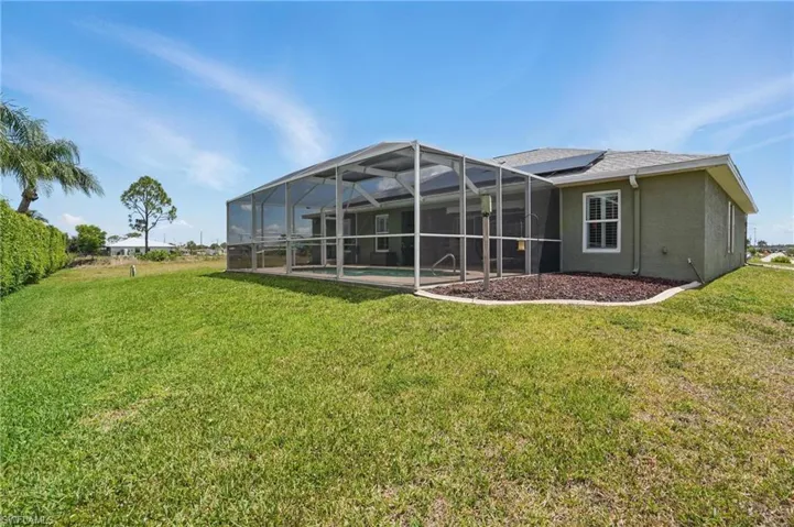 Rear view of house with solar panels, a yard, stucco siding, and a lanai