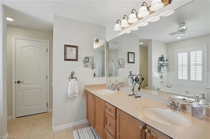 Full bath with tile patterned flooring, a ceiling fan, double vanity, a bath, and baseboards