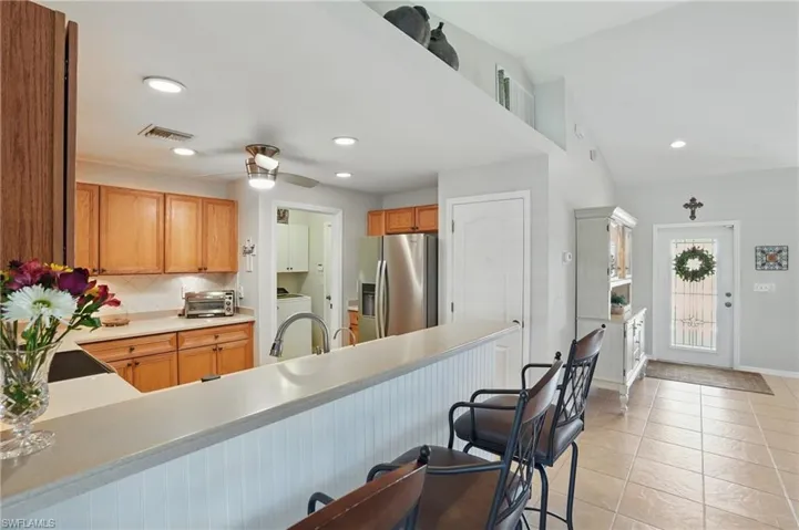 Kitchen featuring stainless steel fridge, a breakfast bar area, decorative backsplash, light countertops, and ceiling fan