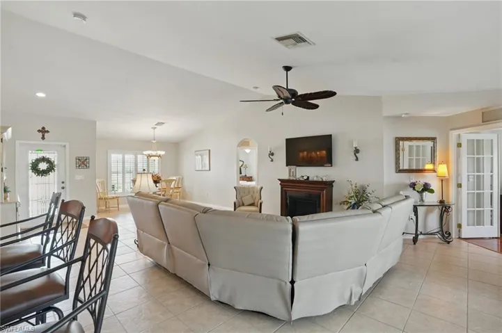 Living room featuring light tile patterned floors, a ceiling fan, vaulted ceiling, a fireplace, and a chandelier