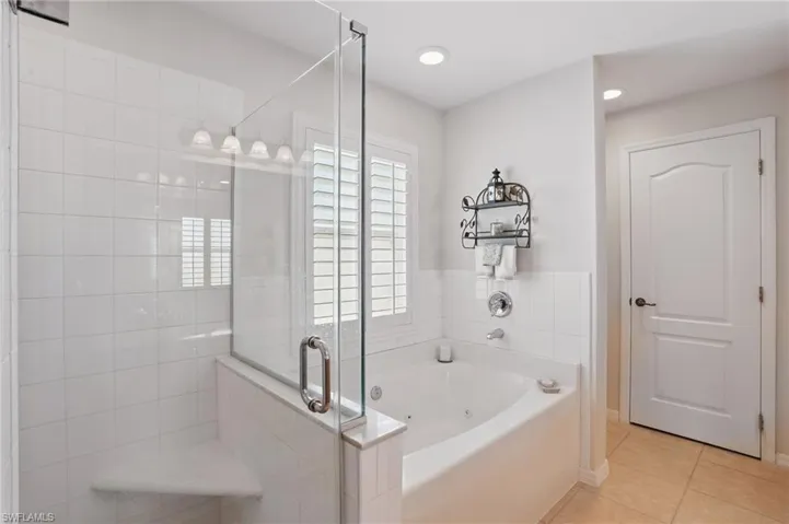 Full bath with tile patterned flooring, a stall shower, a jetted tub, and baseboards