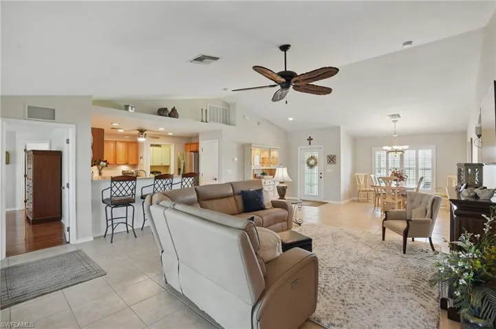 Living room with light tile patterned floors, lofted ceiling, a ceiling fan, a chandelier, and baseboards