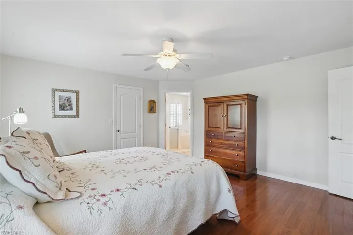 Bedroom with dark wood-style floors, baseboards, ceiling fan, and ensuite bathroom