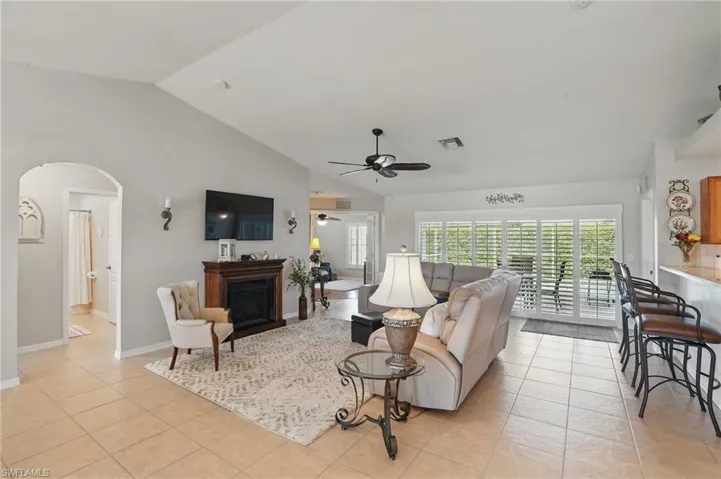 Living room featuring arched walkways, a ceiling fan, a fireplace, light tile patterned floors, and baseboards