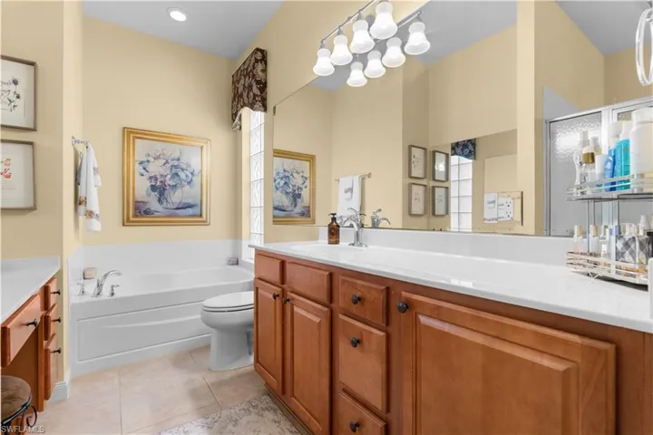 Bathroom featuring wood-finish cabinetry, a large wall-to-wall mirror, an integrated solid-surface countertop, a deep soaking tub, and tile flooring