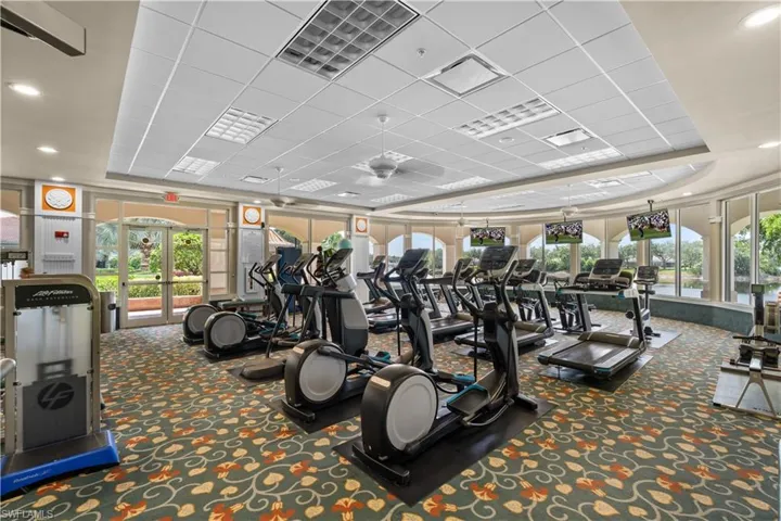 Fitness center featuring a suspended tile ceiling, recessed lighting, expansive glass windows, and dual-door exterior access