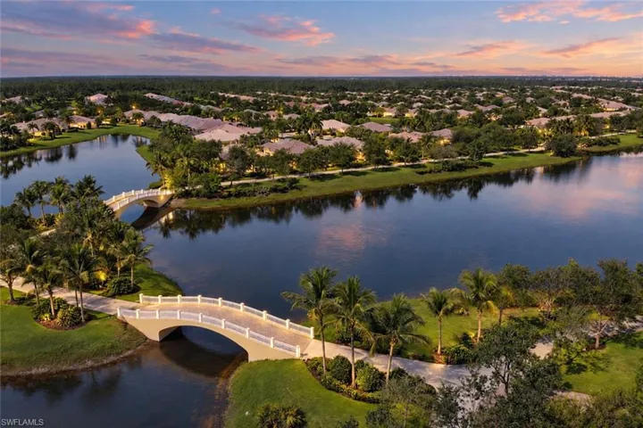 Aerial perspective of a landscaped community featuring expansive water elements, arched pedestrian bridges, paved pathways, and mature palm trees