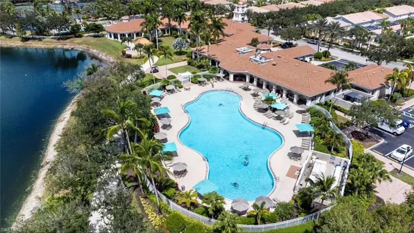 Community clubhouse grounds featuring a large curvilinear swimming pool, expansive paved patio, landscaped perimeter, and proximity to a freshwater lake