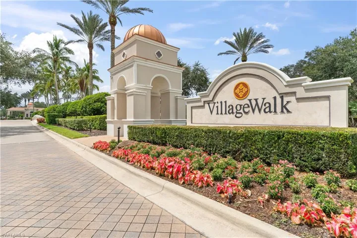 Community entrance featuring a masonry monument sign, copper-capped architectural tower, paver stone roadway, and manicured landscaping