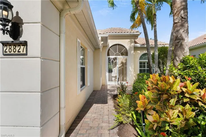 Stucco exterior with decorative quoins, paver walkway, arched entryway with glass-paneled door, and palm-accented landscaping