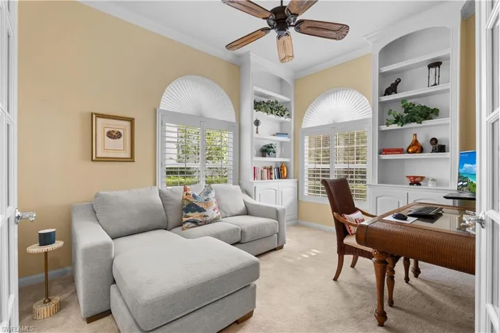 Custom built-in white shelving, arched windows with plantation shutters, crown molding, and a ceiling fan