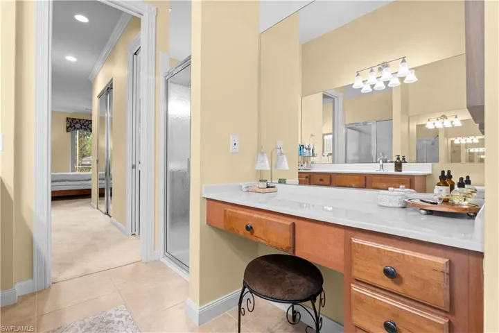 Bathroom featuring a vanity with wood cabinetry, a light-toned countertop, a full-width wall mirror, and a glass-enclosed shower