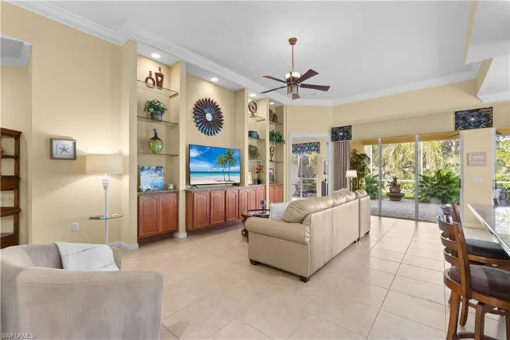 Living area featuring custom floor-to-ceiling built-in cabinetry, crown molding, tile flooring, recessed lighting, and a multi-panel sliding glass door