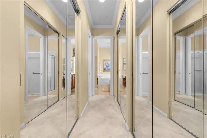 Passageway featuring full-length mirrored sliding closet doors, neutral wall finish, and crown molding