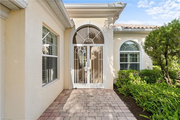 Stucco exterior entrance featuring a paver walkway, arched double entry doors with decorative glass inserts, and arched windows