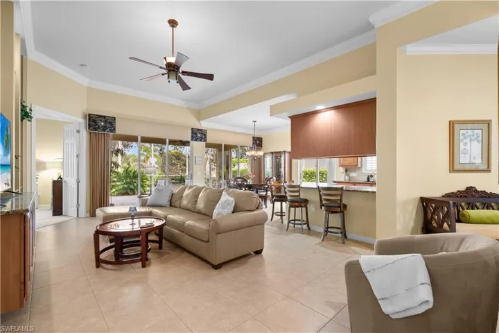 Open-concept interior featuring tray ceilings, neutral tile flooring, expansive sliding glass doors, a kitchen island with stone countertops, and recessed lighting