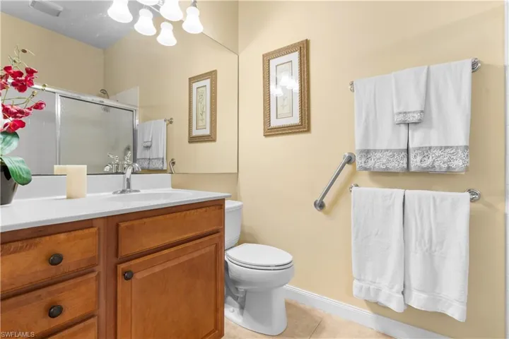 Bathroom featuring a wood-finish vanity with a stone countertop, an integrated sink basin, a multi-light fixture, a wall-to-wall mirror, and a shower enclosure