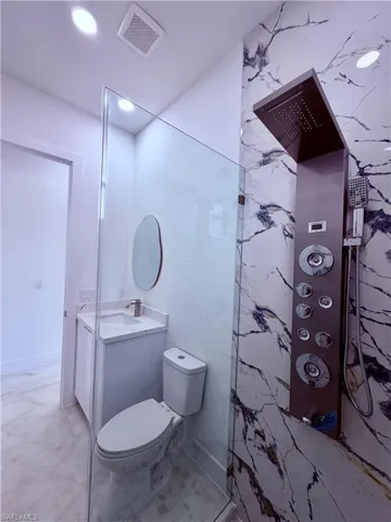 Modern full bathroom featuring a glass-enclosed shower with a multi-function panel, large format marble-look tile, recessed lighting, and a floating vanity with a vessel sink