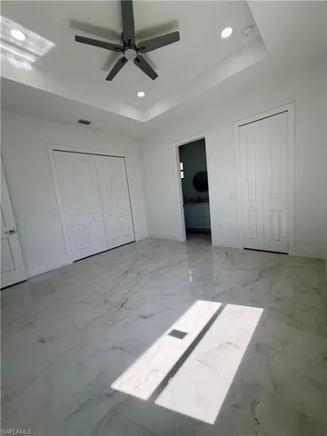 Spacious room featuring large format tile flooring, a tray ceiling with recessed lighting, and a ceiling fan