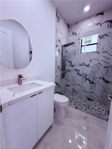 Bathroom featuring a modern vanity with a white countertop and integrated sink, a frameless glass shower enclosure, patterned wall tile, pebble-style shower flooring, and recessed lighting