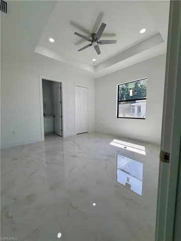 Spacious interior featuring a contemporary ceiling fan, recessed lighting, a tray ceiling, and large format marble-look tile flooring
