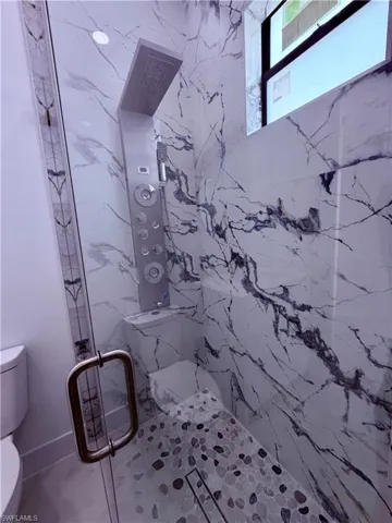 Shower enclosure featuring large format white tiled walls with dark veining, a multi-function shower panel with an overhead rainfall fixture, a built-in shower bench, and a pebble-mosaic floor