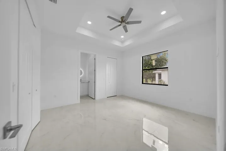 Bright interior space featuring large format tile flooring, a tray ceiling with recessed lighting, and a ceiling fan