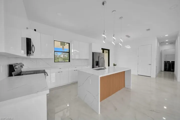 Modern kitchen featuring a waterfall island with wood slat detailing, undermount sink, and three pendant lights