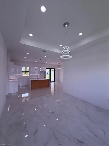 Spacious interior featuring a contemporary multi-ring chandelier, recessed lighting, white walls, glossy tile flooring, and a kitchen island with a wood-finish base