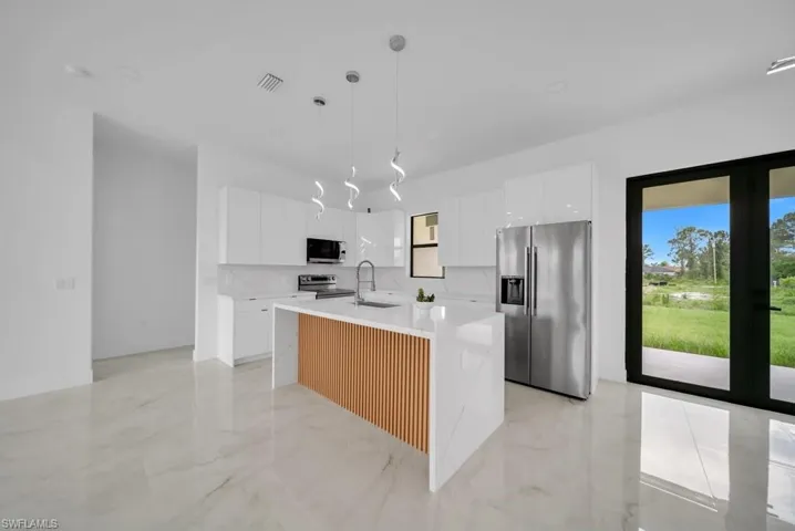 Modern kitchen featuring a waterfall island with wood-slat detailing, white cabinetry, integrated stainless steel appliances, and sleek pendant lighting