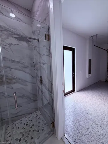 Frameless glass shower with large format marble-effect tile and pebble-style shower pan