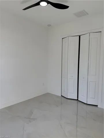 Unfurnished bedroom with light marble finish floors, a closet, and a ceiling fan