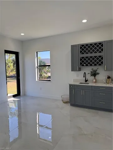 Indoor wet bar with gray cabinetry, recessed lighting, light stone counters, and light marble finish floors