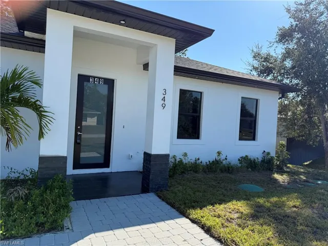 Doorway to property with stucco siding, a yard, and roof with shingles