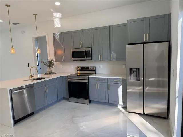 Kitchen with appliances with stainless steel finishes, pendant lighting, a peninsula, light stone countertops, and recessed lighting