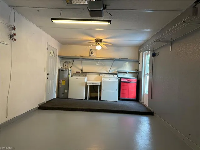 Garage with electric water heater, washing machine and clothes dryer, a garage door opener, and a ceiling fan