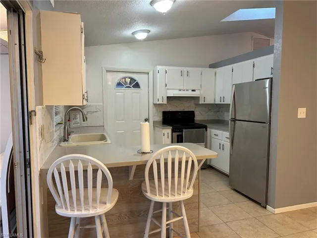 Kitchen with a breakfast bar area, backsplash, stainless steel appliances, a peninsula, and white cabinets