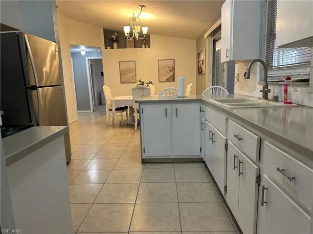 Kitchen featuring light tile patterned floors, freestanding refrigerator, white cabinets, hanging lights, and a peninsula