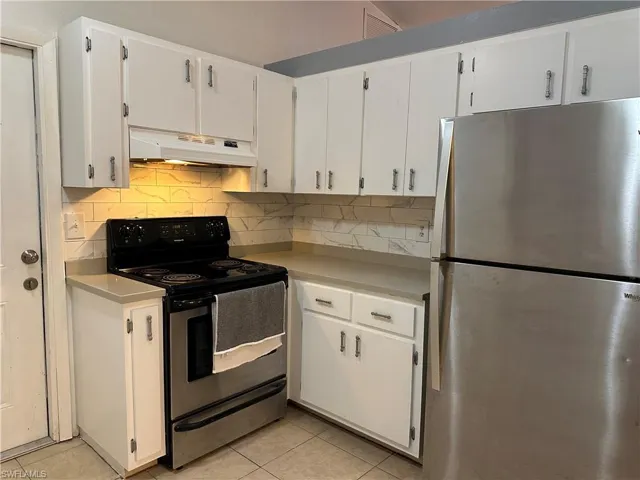 Kitchen with stainless steel appliances, white cabinets, light countertops, light tile patterned floors, and backsplash
