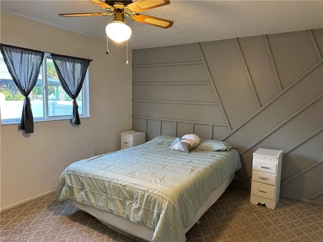 Carpeted bedroom featuring a textured ceiling, ceiling fan, and a decorative wall